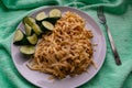 Long and wide pasta spaghetti noodles under viscous melted cheese on a platter with sliced Ã¢â¬â¹Ã¢â¬â¹fresh cucumbers on a bright green